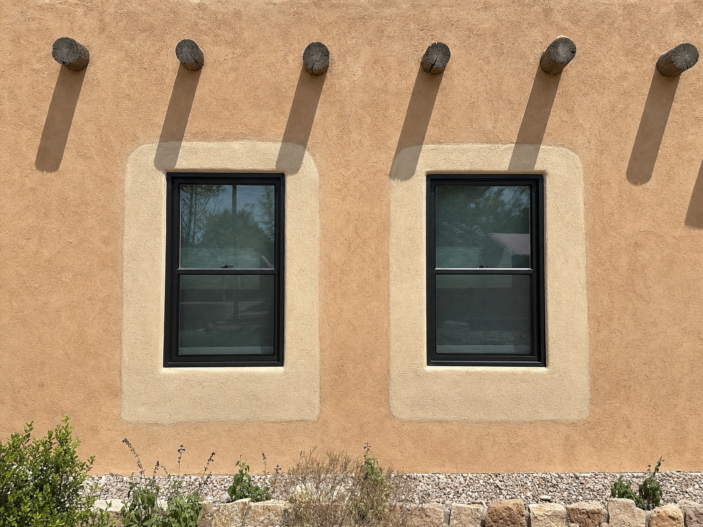 Two windows on a stucco wall with visibly lighter patch outlines around each, showing inconsistent application color