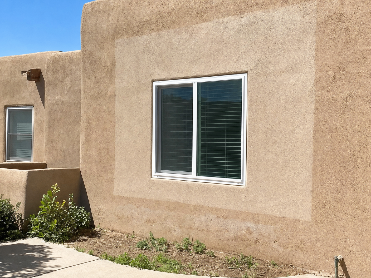 Stucco wall around a new window showing a darker rectangular outline where fresh pigment has not yet oxidized to match the surrounding wall