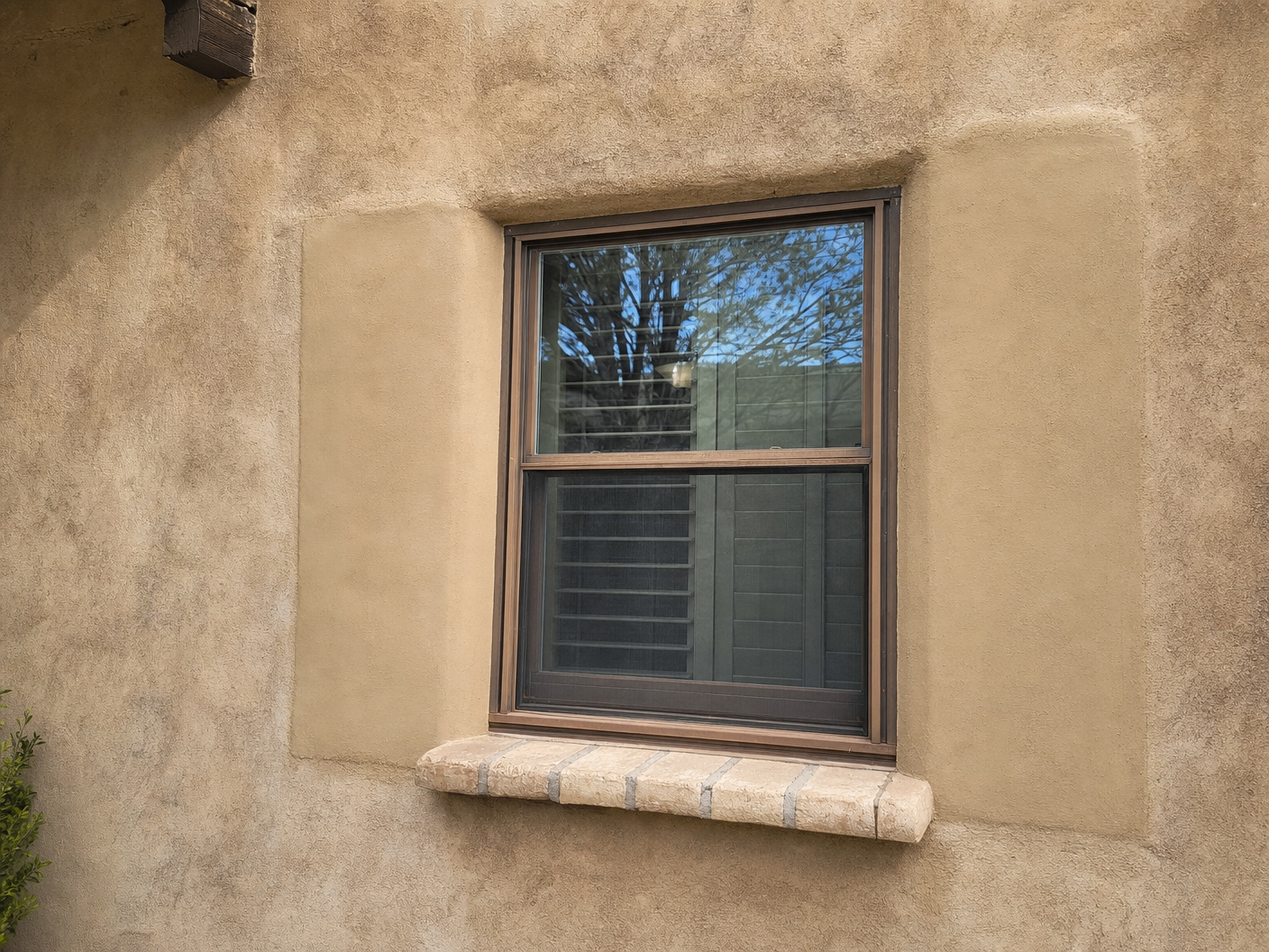 Close-up of a window framed by a fresh stucco patch that is visibly lighter than the surrounding aged stucco wall