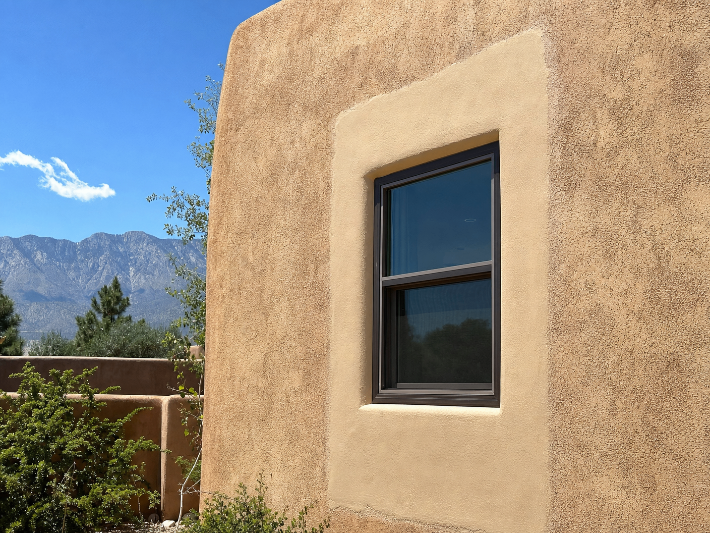 Window surrounded by a smoother, lighter stucco patch on an otherwise weathered adobe-style wall